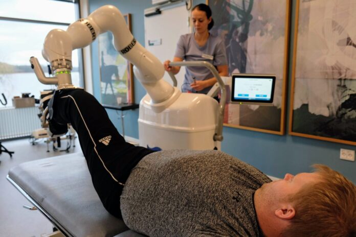 Fysioterapeut Karen Marie Kristensen spænder patientens ben op i robotten Robert, der skal træne musklerne. Foto: Claus Thorhauge.